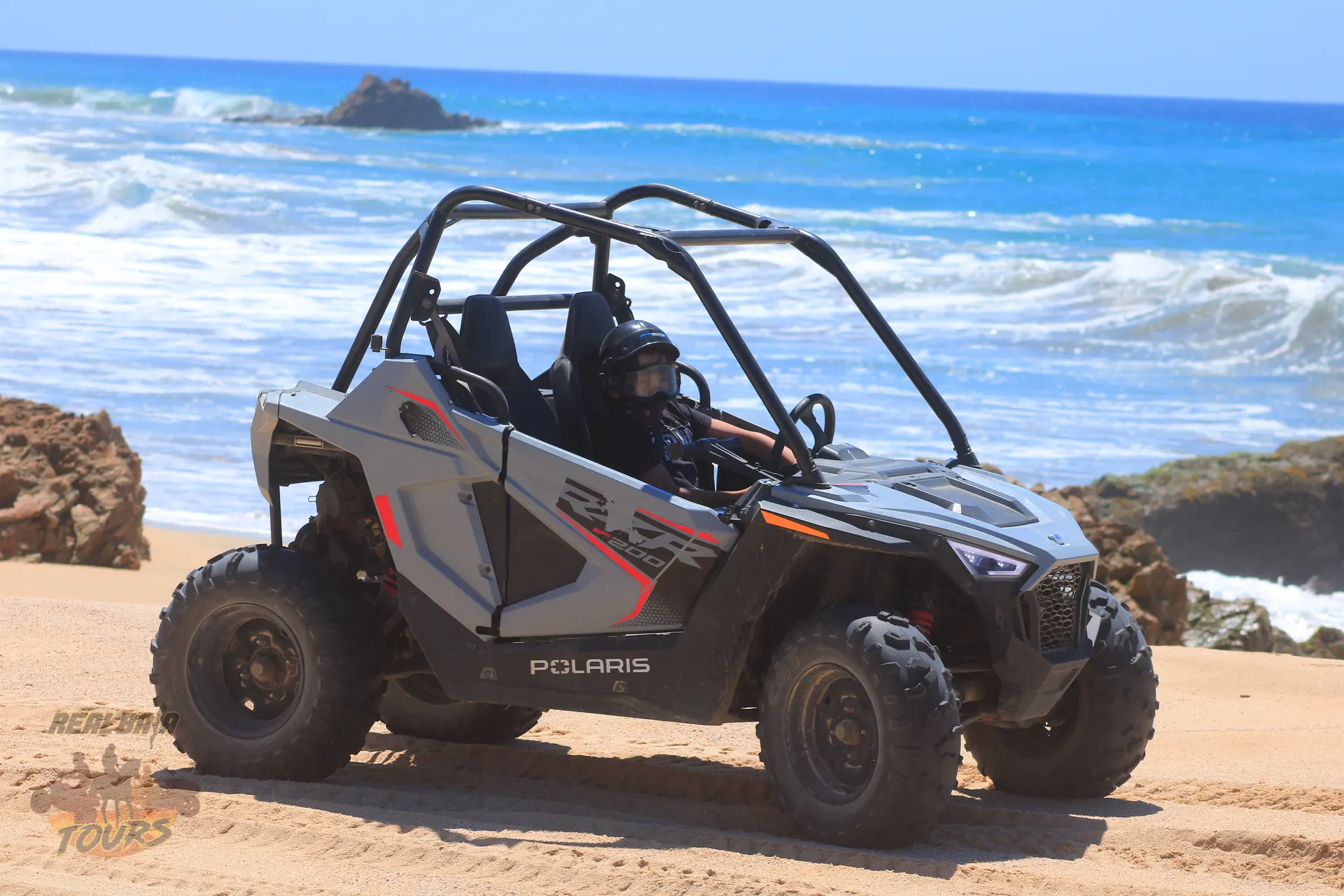 Polaris RZR vehículo lado a lado estacionado en playa de arena with turquoise olas del océano and costa rocosa in Baja California Sur