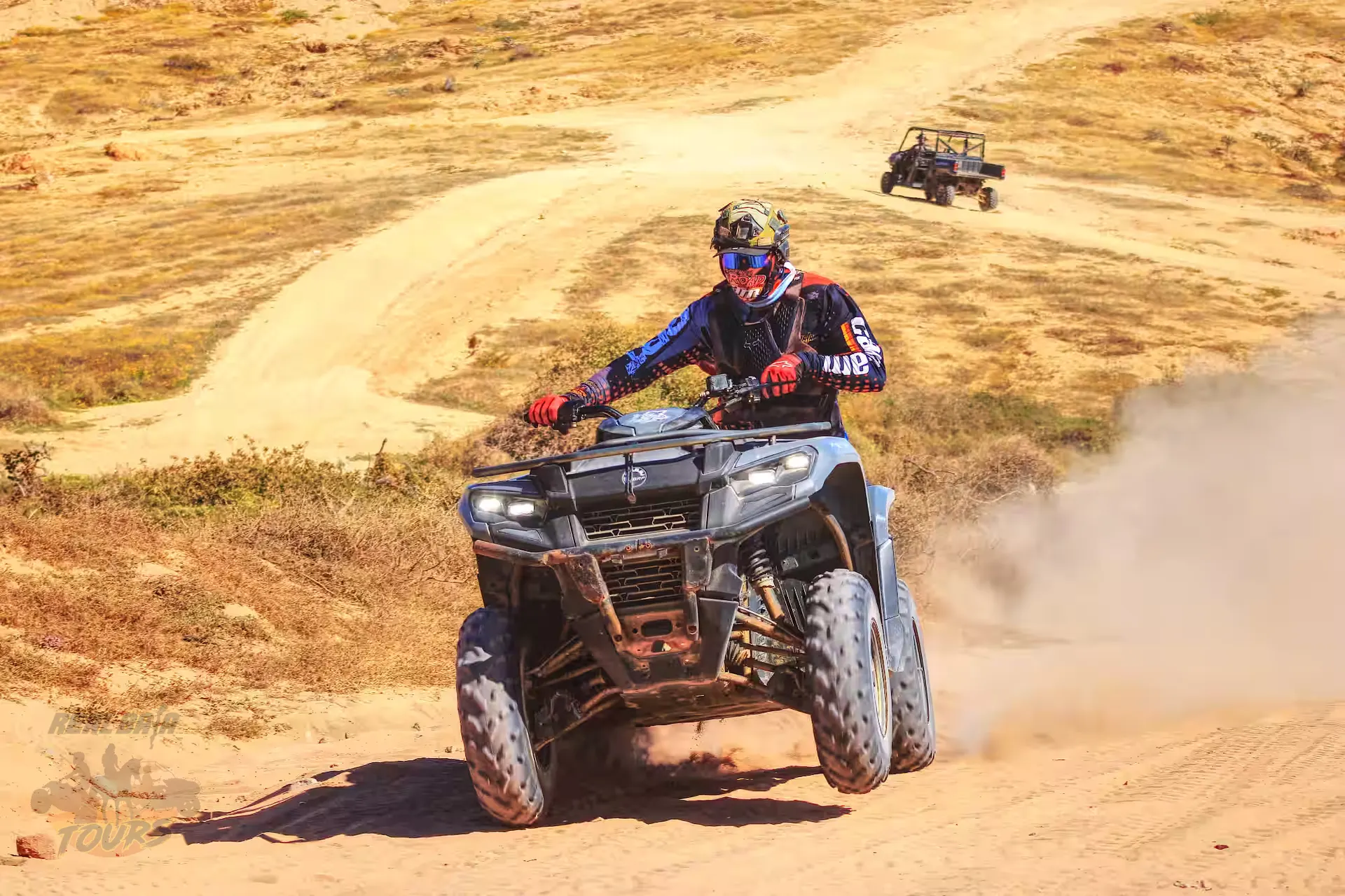 ATV rider kicking up dust on desert trail in Baja California Sur with support vehicle following behind