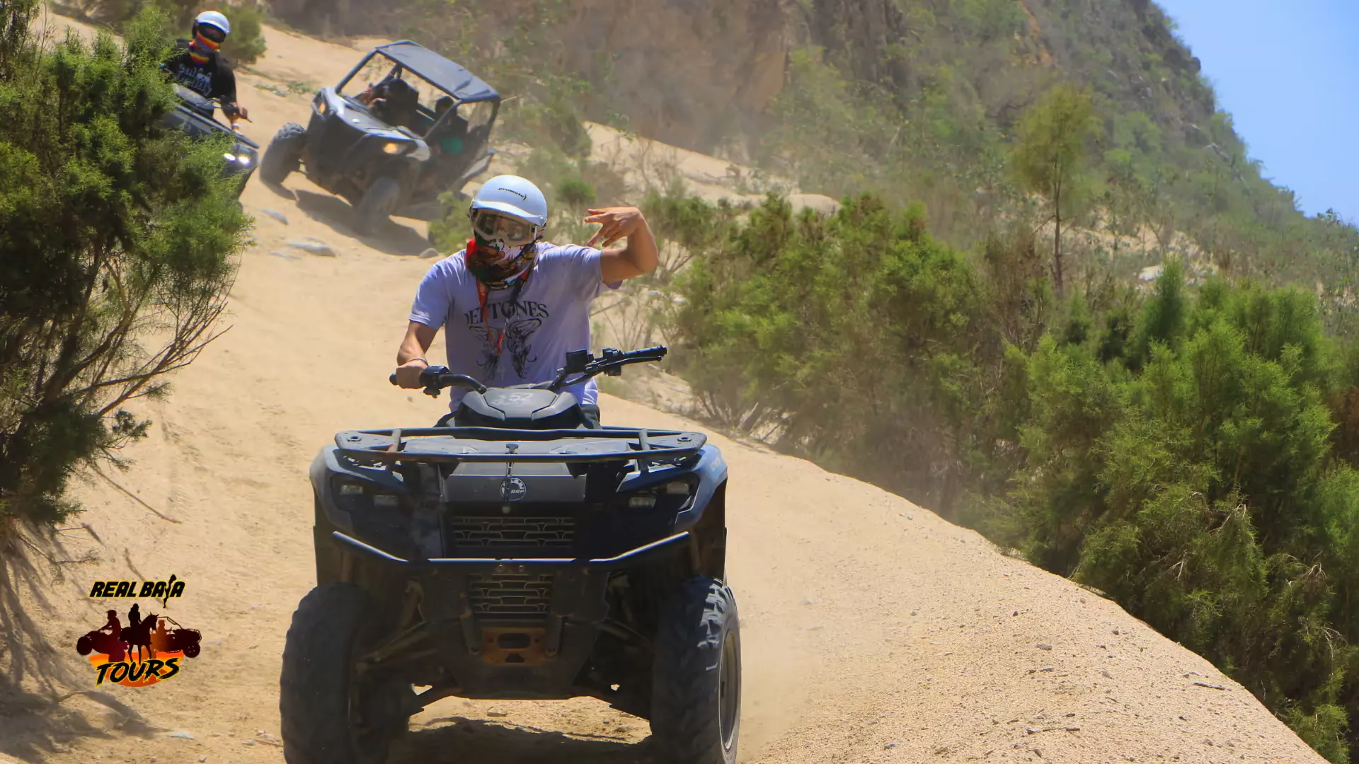 ATV rider on sandy desert trail with rocky cliffs and vegetation in Baja California Sur