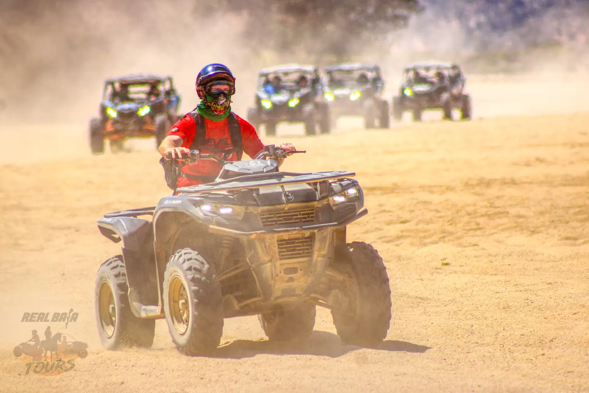 ATV piloto in red shirt leading dust-covered desert convoy on sandy trail in Baja California Sur