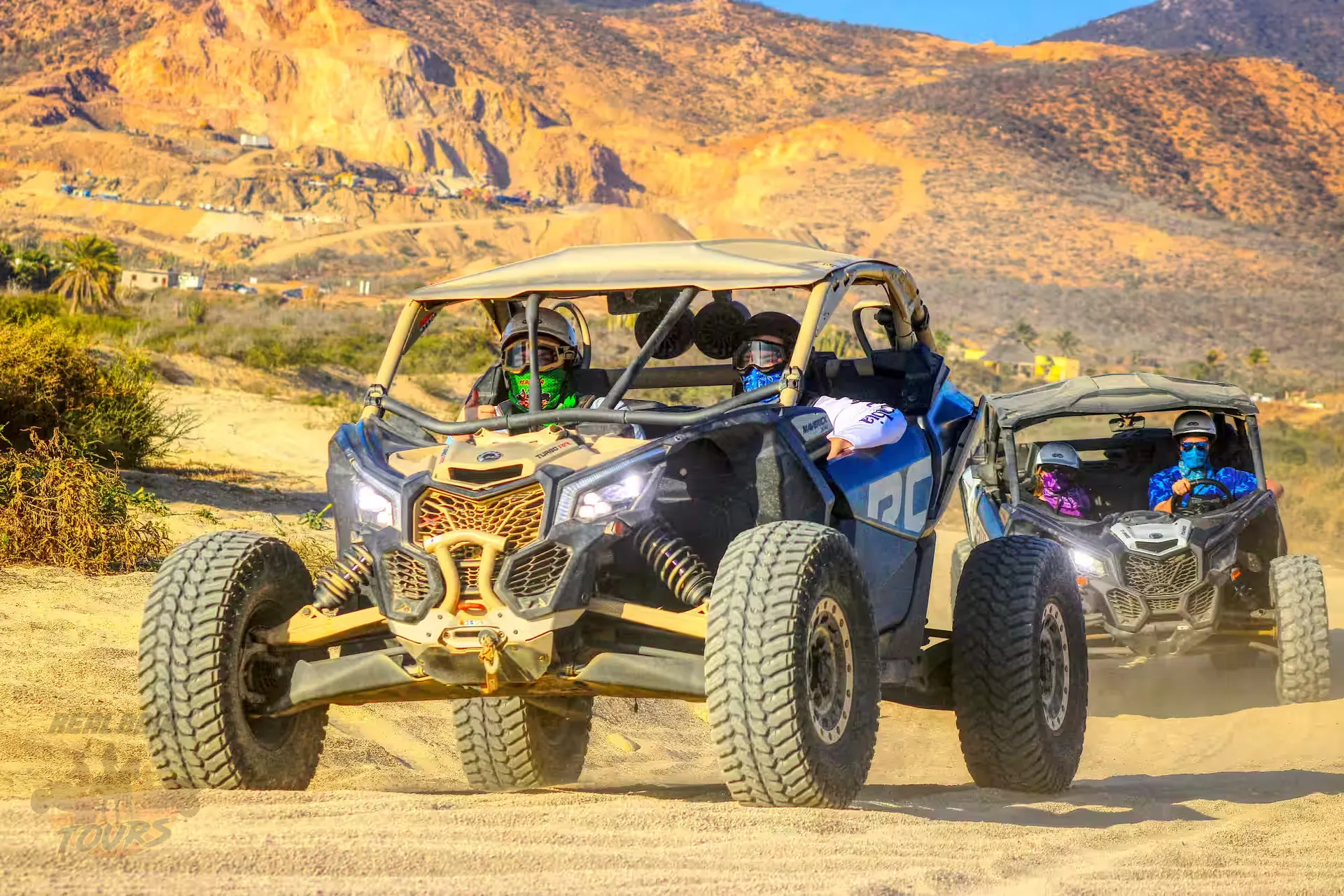 Two off-road buggies with passengers driving through desert terrain with golden mountains in Baja California Sur
