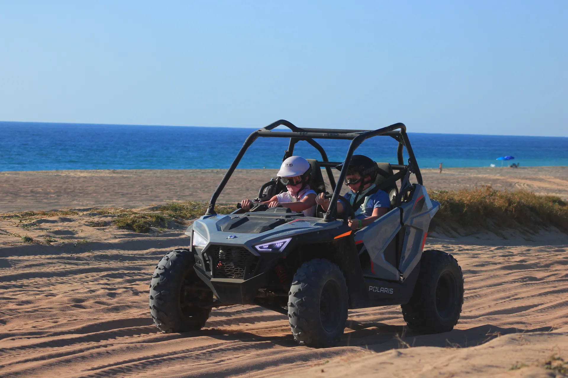 Polaris RZR buggy with two passengers on playa de arena with ocean and blue sky in Baja California Sur