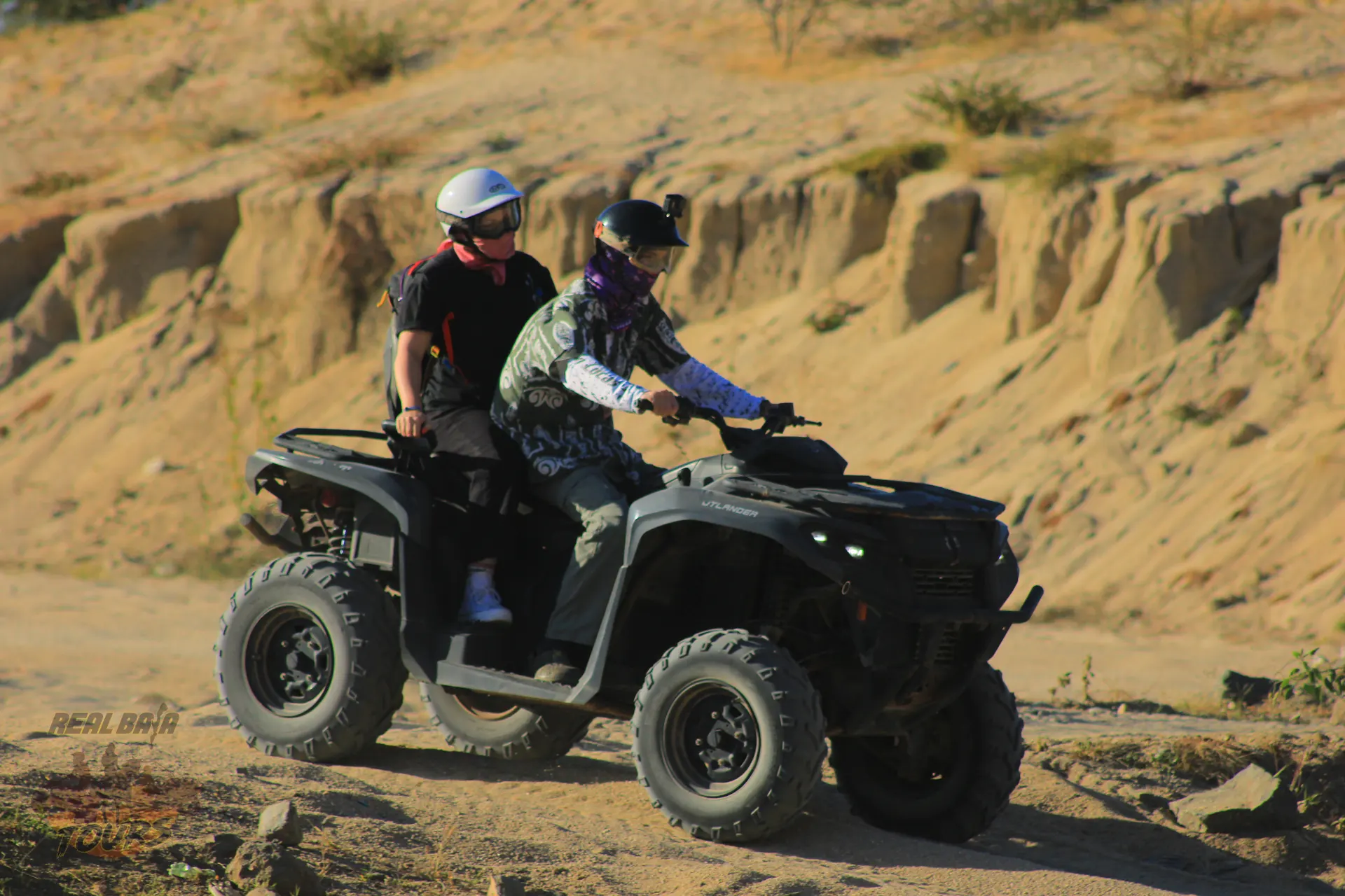 Two jinetes en black Double ATV exploring sandy terreno desértico with eroded canyon walls in Baja California Sur