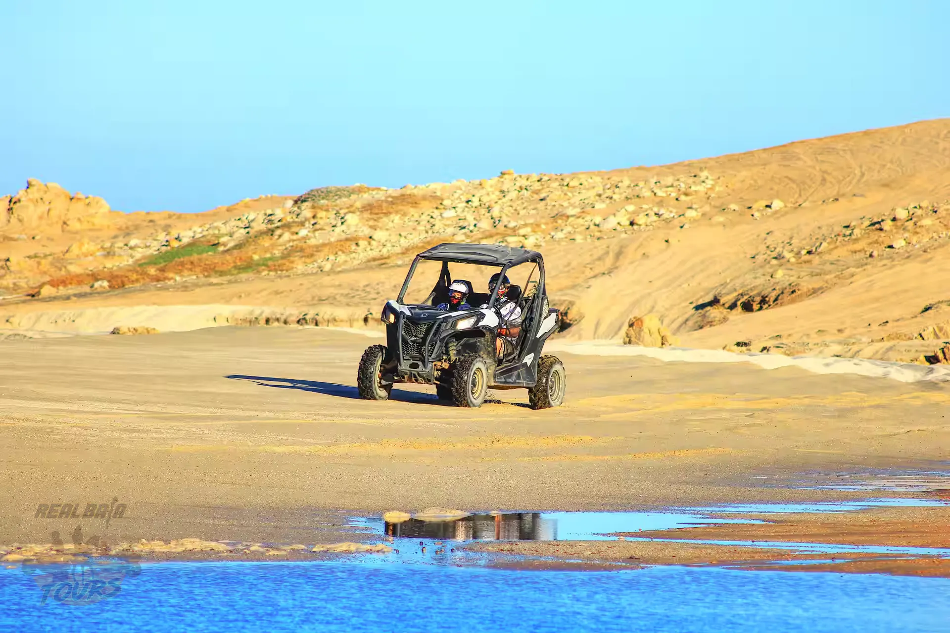 Buggy vehicle with passengers driving on playa de arena near turquoise water in Baja California Sur desert landscape