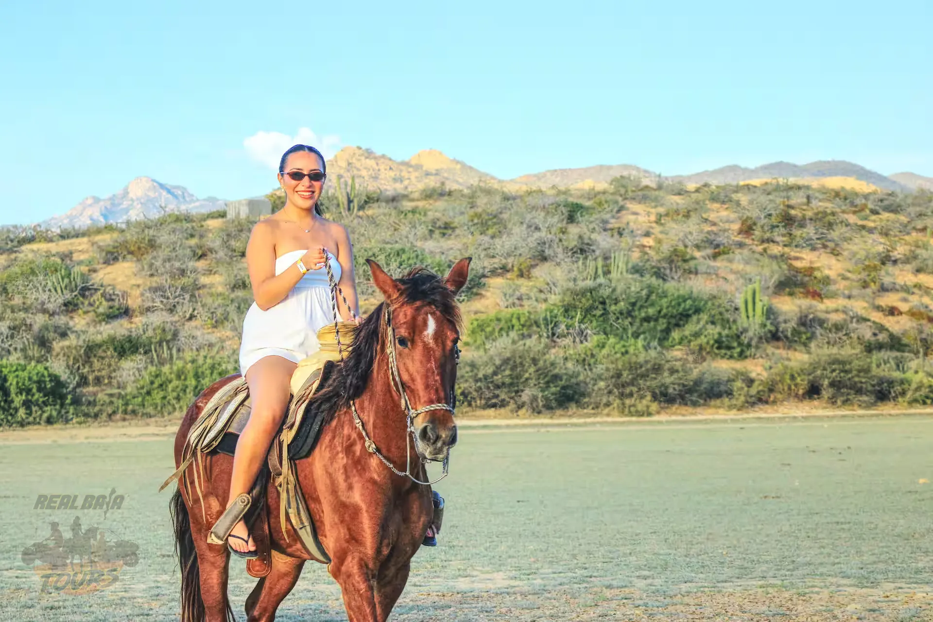 Woman riding brown horse in desert landscape with cacti and mountains in Baja California Sur