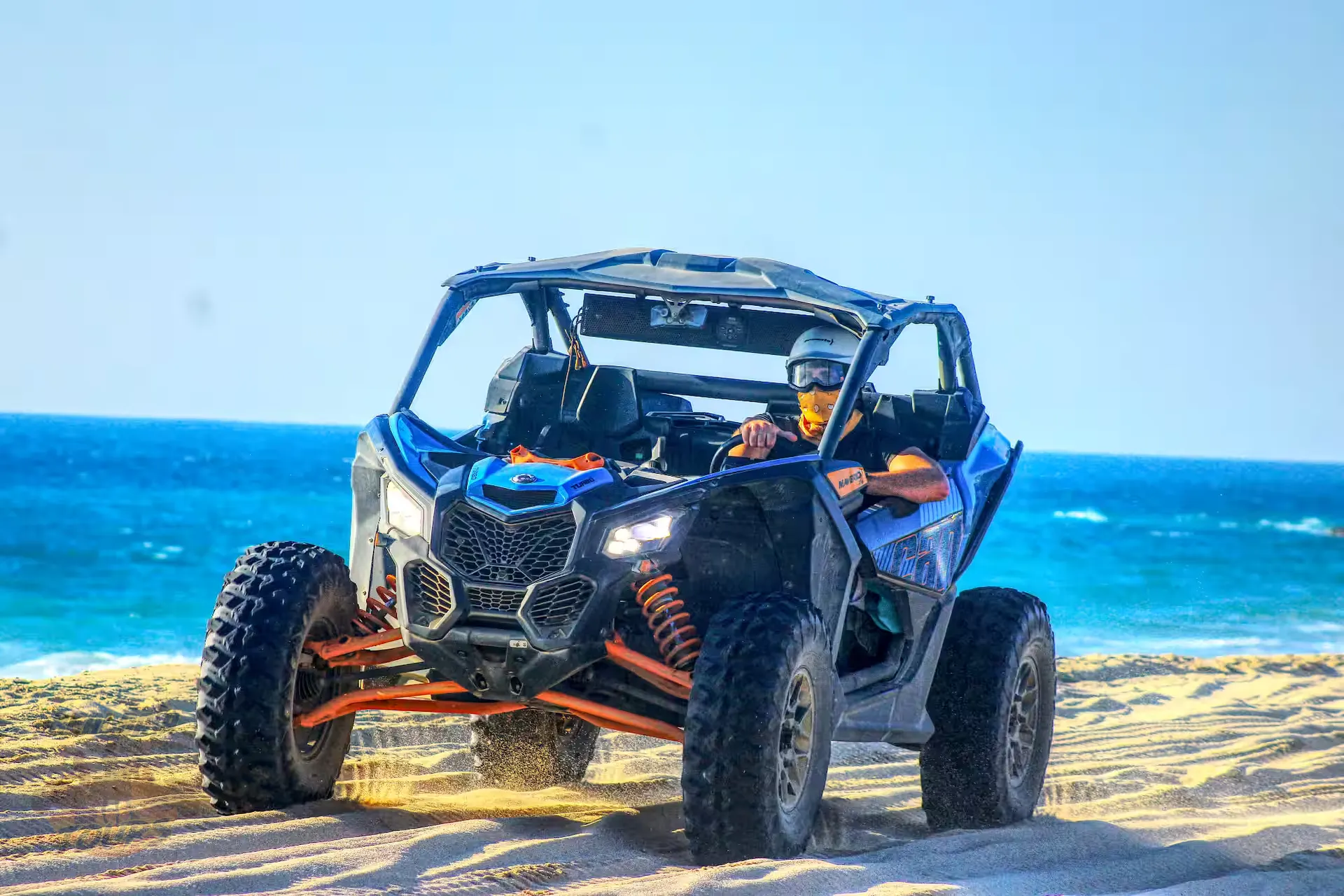 Blue and orange dune buggy with two passengers on a sandy beach with turquoise ocean and clear sky in Baja California Sur Blue and orange dune buggy with two passengers on a sandy beach with turquoise ocean and clear sky in Baja California Sur