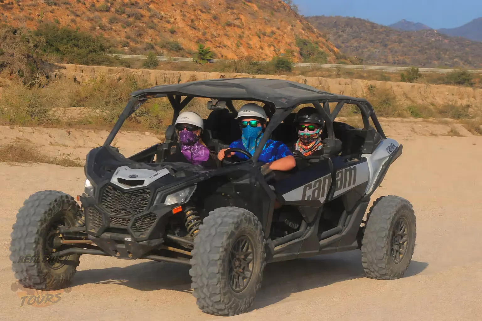 Three adventurers in a Can-Am UTV driving through terreno desértico in Baja California Sur with rocky mountains in background