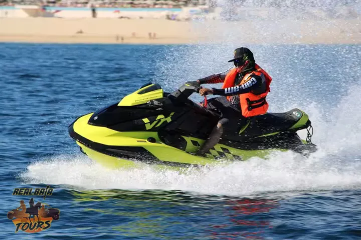 Jet ski rider in neon yellow and black watercraft wearing red life vest, riding waves off Baja California Sur beach