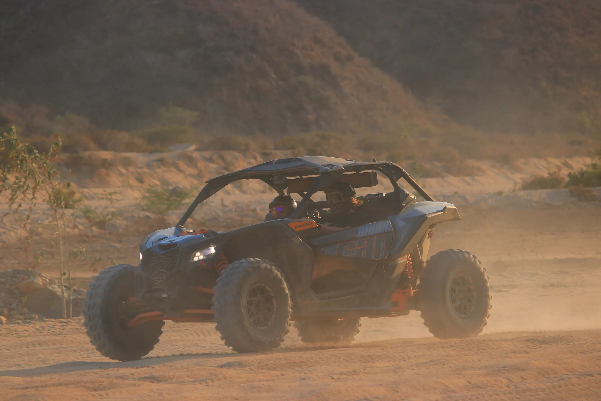 Can-Am X3 Turbo driving through hazy golden-hour dust on a desert trail