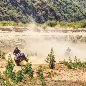ATV rider performing stunt in dusty mud pit with forest backdrop in Baja California Sur adventure tour