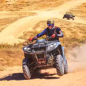 ATV rider kicking up dust on desert trail in Baja California Sur with support vehicle following behind