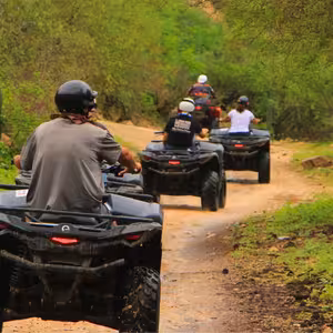 Group of tourists riding black ATVs on a muddy dirt trail through lush green forest in Baja California Sur