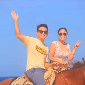 Smiling couple on horseback waving with the ocean behind them