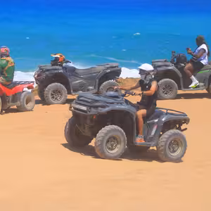 Group of four ATVs parked at a rocky clifftop overlooking bright blue ocean waves