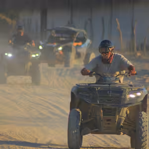 Convoy of ATVs and a UTV riding into a rural village at golden hour