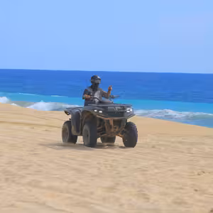 ATV rider flashing a peace sign atop a dune overlooking turquoise ocean water and breaking waves