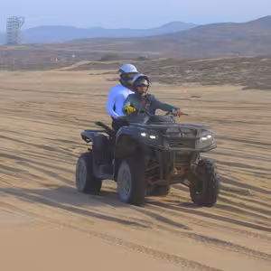ATV with two riders passing a distinctive lookout tower in the desert