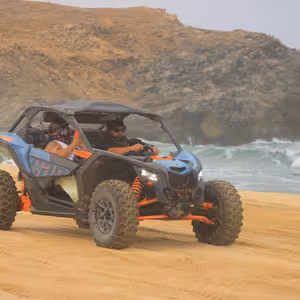 UTV driving along a sandy beach beneath a dramatic rocky headland