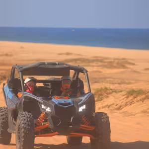 Can-Am X3 buggy parked on a sand dune with turquoise ocean behind