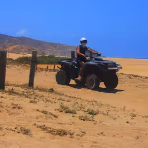 Solo ATV rider cruising a coastal desert trail with mountains and ocean in the background