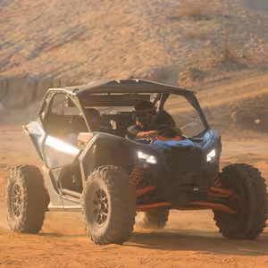 Can-Am X3 Turbo driving through a sandy desert wash at golden hour, headlights on