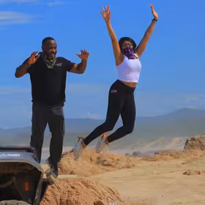 Guide and rider jumping for joy on a rocky outcrop next to their ATV