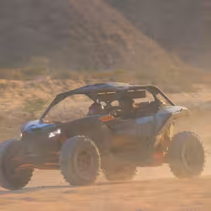 Can-Am X3 Turbo driving through hazy golden-hour dust on a desert trail
