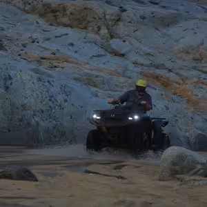 ATV splashing through water among large granite boulders