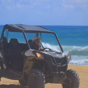 Single UTV parked on the beach with turquoise waves breaking behind it, driver in helmet and goggles