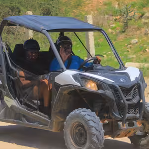 Two riders in a UTV waving cheerfully on a dusty desert trail near Candelaria