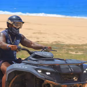 ATV rider driving along the beach with blue ocean behind