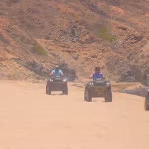 Group of ATV riders crossing a sandy wash between colorful desert hills