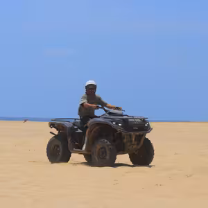 ATV rider crossing an open sandy beach with the ocean on the horizon