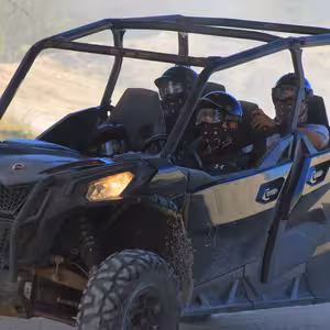 Four riders in a UTV with helmets and bandanas driving through dust on a desert trail