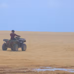 ATV rider on a vast open beach with tide pools in the foreground