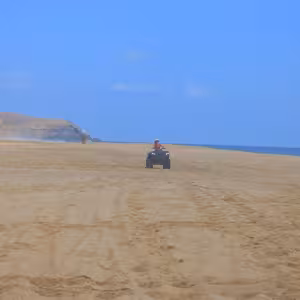 ATV rider on a wide sandy beach with a rocky point in the distance