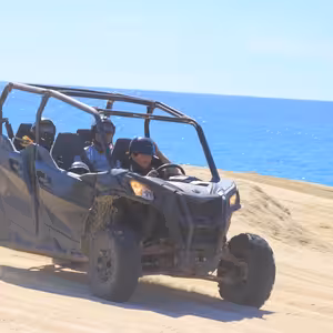 Four riders in a UTV driving along a sandy bluff above the open ocean