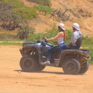 Two riders on an ATV passing cactus-covered hillsides
