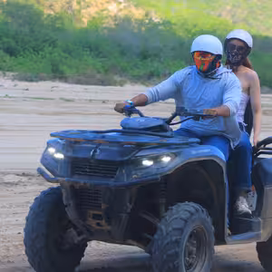Couple riding double on an ATV through green desert scrub