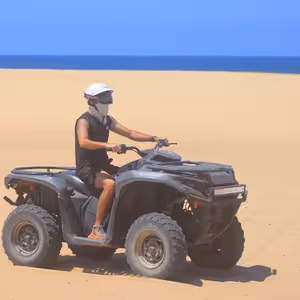 Solo ATV rider crossing an open beach with a clean turquoise ocean horizon behind him
