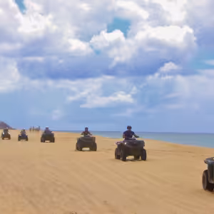 Group of ATV riders on a sandy beach in Baja California Sur with ocean and cloudy sky