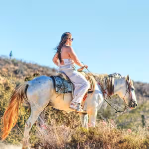 Woman in white outfit riding a palomino horse on a desert trail in Baja California Sur with cacti and mountains