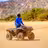 ATV piloto in blue jacket on dusty sendero del desierto with rocky hillside and green vegetation in Baja California Sur